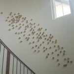 Professional art installation of metal gold wall art descending with the stairs - Art Hangers
